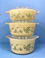 Stacked view of three vintage Pyrex casserole bowls in Shenandoah design, showing olive green floral pattern on cream background with clear lids on top.