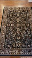 Full view of the dark blue area rug with intricate light floral patterns and border on wood floor