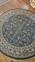 Photo showing the full round dark blue rug with floral patterns and a multi-layered border on a wooden floor.