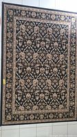 Full view of the rectangular area rug showing the entire black and tan floral and vine design with ornamental borders.