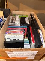 Box with assorted audio cassette tapes, music CDs, DVD movie cases, and other audio-related items