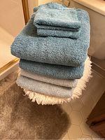 Stacked towels in blue and gray on top of a fringed bath mat on tiled floor