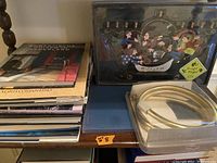 Table surface with stacked books, menorah displayed behind protective cover, and coiled tubing in plastic packaging.