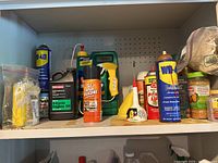 Shelf with multiple chemical containers including WD-40, engine oil, silicone spray, and other garden-related maintenance products.