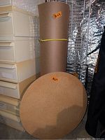Photo of a round cork board tabletop, large roll of brown construction paper, and metal wire racks stored in a garage.