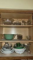 Wooden shelf with multiple glass and ceramic dishware items including bowls, plates, cups, and a set of salt and pepper shakers