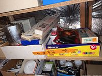 Box containing multiple household items such as light bulbs, cords, sports net, and storage boxes.