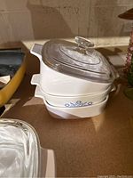 Stacked white CorningWare baking dishes with blue floral design and clear glass lids.