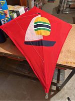 Red diamond-shaped kite with colorful sailboat design, shown front and back showing wooden frame and string.