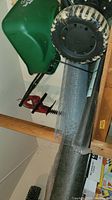 Green turf builder spreader with rear wheels and handle, leaning against wall.