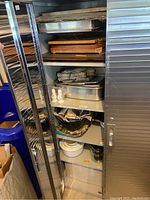 Open metal storage cabinet showing multiple shelves inside with baking trays and kitchen items (contents not included).