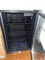 Interior view of mini fridge showing multiple black wire shelves, temperature control knob on top inside, and blue interior lighting.