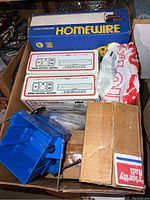 Cardboard box containing several boxes of Southwire Homewire electrical wire, blue plastic electrical boxes, and other electrical parts.