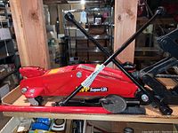 Photo shows red MVP SuperLift hydraulic floor jack with black handle and wheels on a wooden shelf.