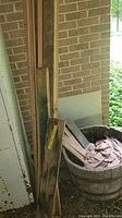 Wood pieces leaning against brick wall beside wooden barrel planter with fabric inside