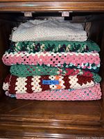 Stack of various knitted and crocheted quilts in different colors on a wooden surface.