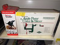 Both boxes shown side by side on shelf, showing the KitchenAid rotary grater box and White Mountain Apple Corer & Slicer box.