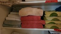 Shelves stacked with different colored towels including beige, red, gray, white, and green patterned towels.