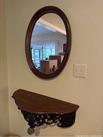 Wall shelf and oval mirror mounted on a wall, showing the detailed carved supports and smooth wood finish of the shelf with the matching framed mirror above.