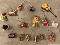 Photo of 16 assorted miniature Christmas tree ornaments on a gray surface showing various holiday designs including Matryoshka dolls, rocking horses, gifts, guitar, angel, stocking, house, gingerbread man, and toy train.