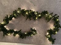 Artificial pine garland with warm white mini lights laid out on carpet, illuminated to show lighting function.