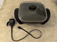 Top-down image of the Black & Decker electric skillet with attached temperature control probe, glass lid in place, and power cord visible.