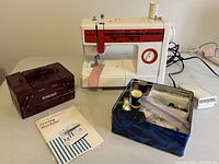 Photo showing Brother sewing machine, vintage Singer wooden sewing chest, metal box with sewing supplies, and user manual on table