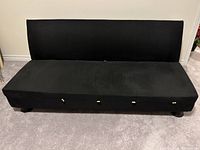 Front view of the futon sofa bed in sofa position showing black-brown microfiber upholstery with visible short legs on carpeted floor.