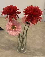 Glass vase filled with 2 red and 2 pink artificial flowers on a table