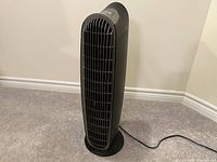 Full side view of black Honeywell tower air purifier showing front air vent grille and base on carpeted floor.