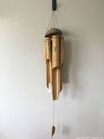 Full view of the bamboo wind chimes hanging, showing four bamboo tubes with natural color and carved openings at the bottom, suspended from a rounded top cap.