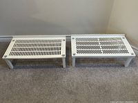 Two white stackable shoe shelves side by side on a carpeted floor.