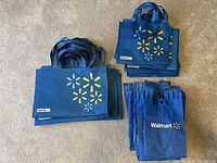 Photo shows stacked large, medium, and small Walmart reusable shopping bags in blue with logo and starburst design.