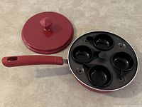 Photo of red nonstick egg poacher pan showing four circular egg molds inside and the matching lid placed next to it.
