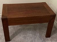 Front angle view of the reddish brown solid wood side table showing the wood grain and joinery details on the corners.
