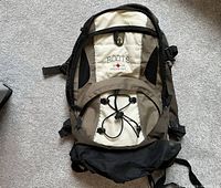 Front view of Roots branded backpack showing exterior pockets, bungee cord, and logo