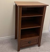 Front view of Sauder media cabinet showing three shelves and bottom drawer closed.