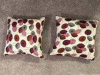 Photo showing two square pillows with contemporary floral prints on a neutral carpet surface.