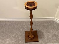 Front angled view of vintage handcrafted wooden ashtray stand showing the carved tubular column, round base on square platform, and recessed top ashtray area.