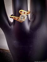 Ring displayed on a black mannequin hand showing the front view of the bypass design and central solitaire.