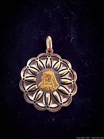 Front view of the round yellow gold pendant showing the open filigree design and central embossed saint motif.