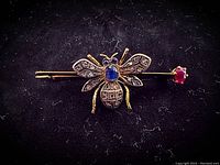 Full front view of the bee brooch and ruby-tipped bar pin on black background