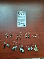 7 pairs of silver earrings plus single amber earring arranged on flat surface with lot label