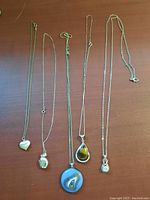 Five silver chains laid flat with pendants visible, including a notable large blue agate pendant and a heart pendant.