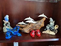 Full view of the collection showing blue glass birds, red glass birds, white ceramic dolphins on wooden base, black and beige ceramic birds, and a detailed ceramic budgie bird on branch.