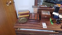Image of assorted items on wooden dresser, including wood boxes, tic tac toe game, brass dish, and clock box.