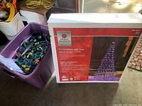 Photo showing a purple plastic bin filled with various outdoor Christmas light strings and the boxed 5 ft Twinkling LED Tree by Home Accents Holiday.