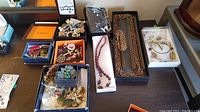 Photo showing multiple boxes containing costume jewelry including earrings, pins, necklaces, and brooches arranged on a table.