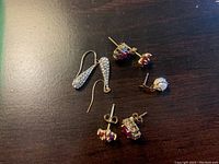 Photo showing three pairs of gold earrings and one single stud earring on dark wood surface.