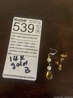 Photo of the lot with MaxSold tag showing 14k gold noting and three earrings displayed on a dark surface.
